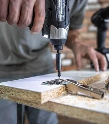 someone drilling into composite board, potentially assembling a desk